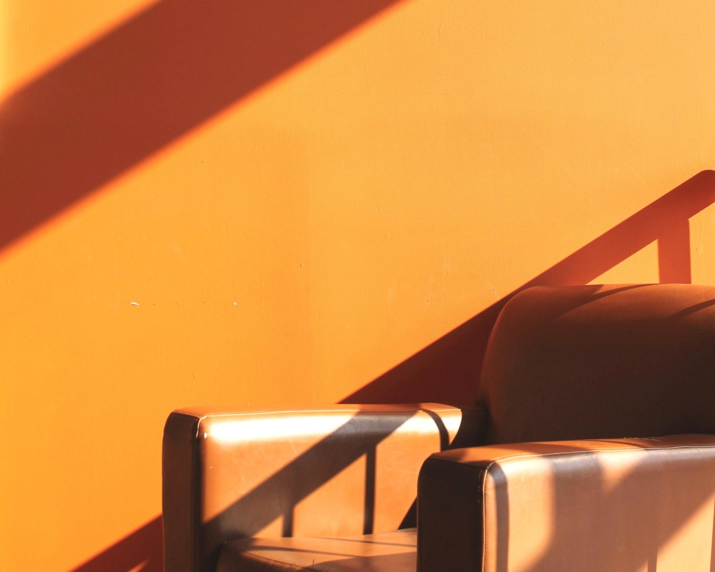 Two leather armchairs against a bright orange wall, cut by a diagonal band of afternoon sunlight.